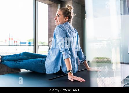 Lächelnde junge Geschäftsfrau, die im Büro auf dem Schreibtisch sitzt Stockfoto