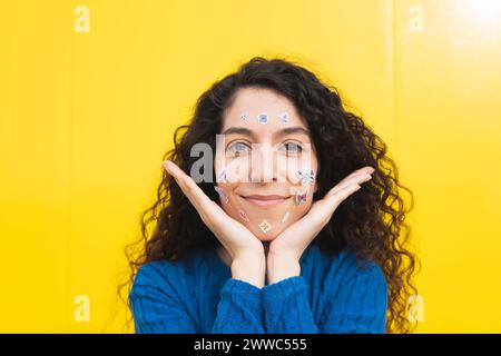 Lockige Frau mit Aufklebern im Gesicht vor gelbem Hintergrund Stockfoto