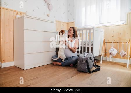 Glückliche schwangere Frau, die mit Hund im Kinderzimmer zu Hause spielt Stockfoto