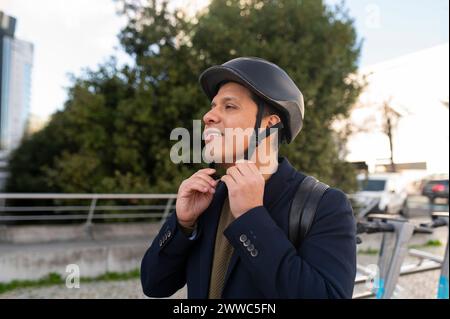 Lächelnder Geschäftsmann, der den Helm vor dem Baum justiert Stockfoto