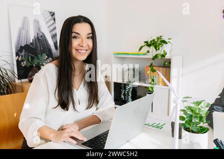 Glückliche junge Geschäftsfrau sitzt mit Laptop im Büro Stockfoto