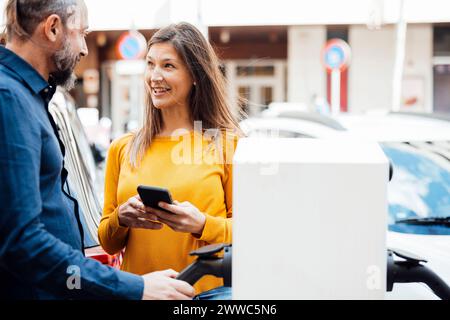 Glückliches Paar, das an der Ladestation für Elektrofahrzeuge spricht Stockfoto