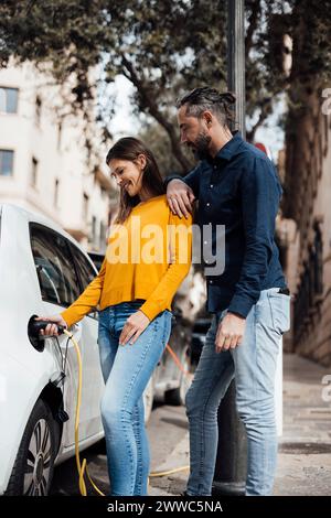 Lächelndes Paar, das das Auto mit einem Elektrostecker auflädt Stockfoto