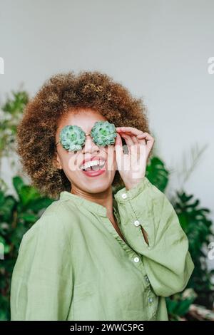 Glückliche junge Frau, die eine Brille mit Blumen aus saftiger Pflanze trägt Stockfoto