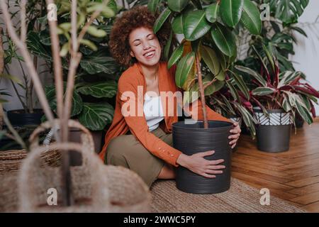 Glückliche Frau, die mit Pflanzen auf dem Teppich sitzt Stockfoto