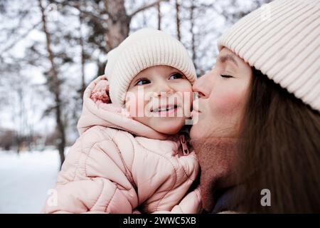 Junge Mutter küsst Tochter im Winterpark Stockfoto