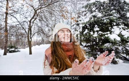 Fröhliche Frau, die im Winterpark mit Schnee spielt Stockfoto