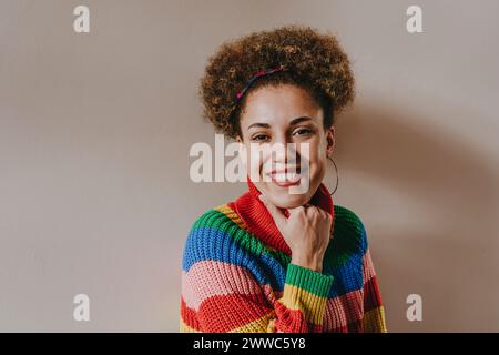 Glückliche Frau, die einen mehrfarbigen Pullover vor der Wand trägt Stockfoto