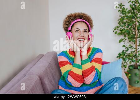 Glückliche junge Frau, die Musik über Kopfhörer auf dem Sofa zu Hause hört Stockfoto