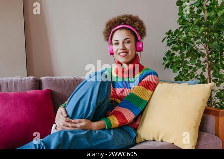 Glückliche Frau, die kabellose Kopfhörer trägt und auf dem Sofa sitzt Stockfoto