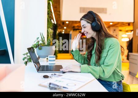 Glückliche Geschäftsfrau winkte bei Videoanrufen am Schreibtisch im Büro Stockfoto