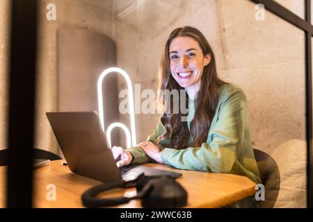 Glückliche, reife Geschäftsfrau, die mit Laptop im Büro sitzt Stockfoto