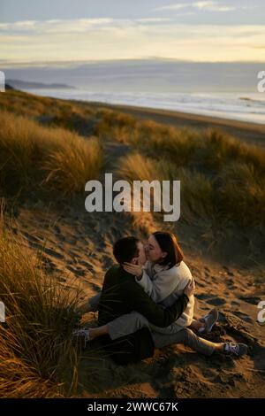 Junge Frau, die am Strand ihren Freund küsst Stockfoto