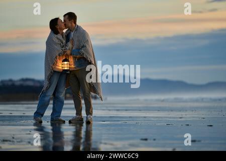Junger Mann mit Laterne, der eine Freundin am Strand küsst Stockfoto