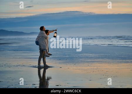 Frau, die am Strand am Meer mit Huckepack auf Mann reitet Stockfoto
