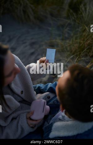 Ein junges Paar, das sich am Strand einen Fotodruck ansieht Stockfoto