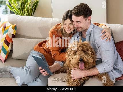 Glückliches junges Paar mit Tablet-PC und mit Hund auf Sofa im Wohnzimmer Stockfoto