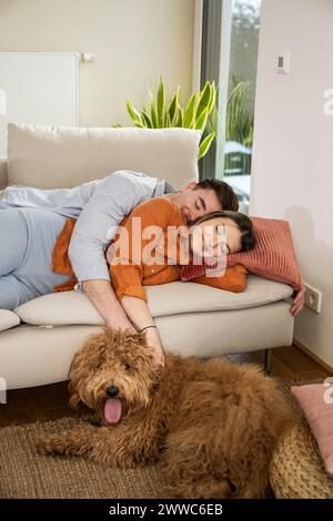 Ein junges Paar, das auf dem Sofa neben dem Hund zu Hause schläft Stockfoto