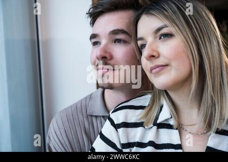 Junges Paar, das zu Hause durch das Fenster schaut Stockfoto