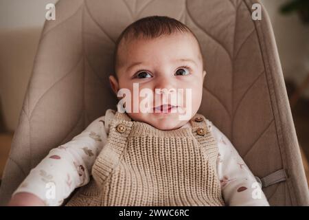 Glückliches süßes Mädchen, das auf beigefarbenem Prahlstuhl sitzt Stockfoto