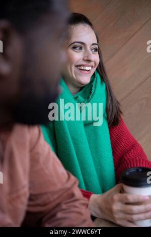 Glückliche Frau, die einen Schal trägt, sitzt in der Nähe des Mannes im Café Stockfoto
