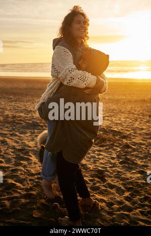 Junger Mann, der glückliche Frau am Strand trägt Stockfoto