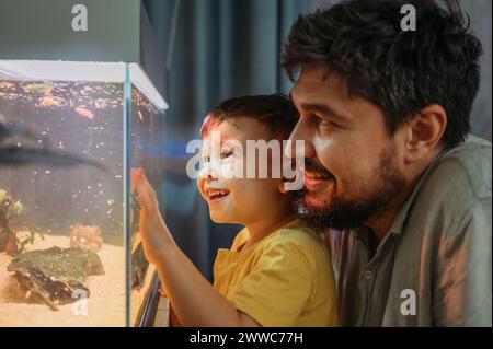 Glücklicher Junge, der Fische im Tank mit Vater zu Hause beobachtet Stockfoto