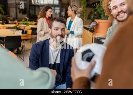 Geschäftsmann, der einen Kollegen ansieht, der Fußball im Büro hält Stockfoto