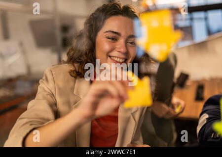 Lächelnde Geschäftsfrau, die zu Hause Haftnotizen an die Glaswand klebt Stockfoto