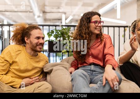 Geschäftsfrau mit lockigen Haaren, die im Co-Working-Raum unter Kollegen sitzt Stockfoto