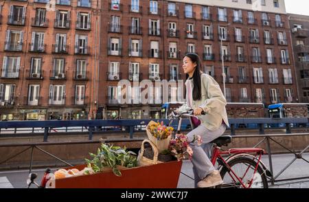 Lächelnde junge Frau, die mit dem Lastenrad in der Nähe des Gebäudes in der Stadt fährt Stockfoto