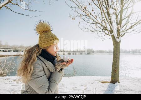 Frau mit herzförmigem Schneeball in der Hand in der Nähe des Sees Stockfoto