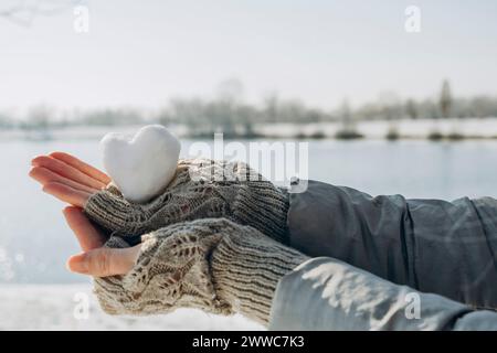 Hände einer Frau, die einen herzförmigen Schneeball in der Nähe des Sees hält Stockfoto