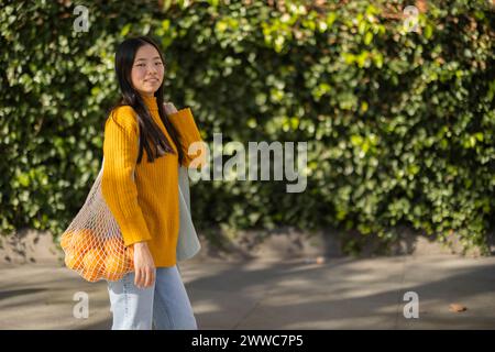 Lächelnde Frau, die mit einem Beutel Orangen in der Nähe von Pflanzen steht Stockfoto