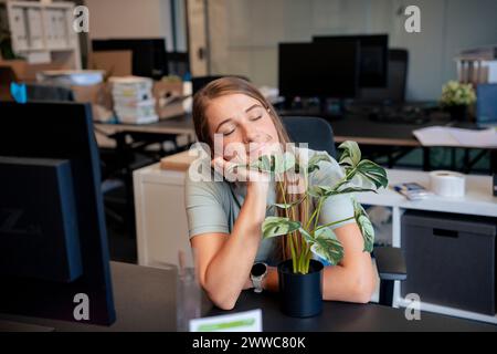 Sorglose Geschäftsfrau, die in der Nähe von Topfpflanzen am Schreibtisch im Büro ruht Stockfoto