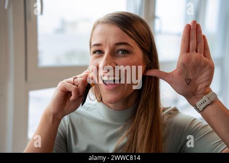 Fröhliche Geschäftsfrau, die im Büro das Herz auf der Palme zeigt Stockfoto