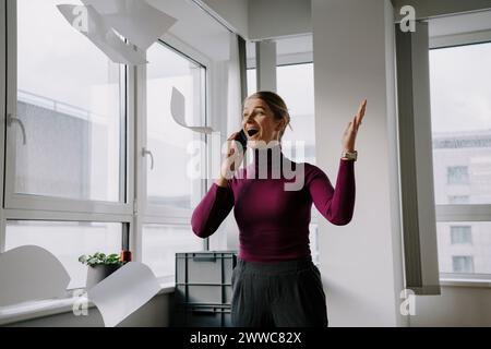 Eine aufgeregte Geschäftsfrau, die im Büro Papiere in die Luft wirft Stockfoto