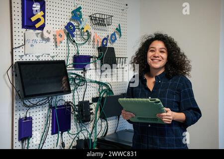 Lächelnder Ingenieur, der den Tablet-PC hält und in der Nähe von Netzwerkkabeln auf der Platine steht Stockfoto