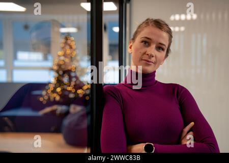 Junge Geschäftsfrau, die sich im Büro an eine Glaswand lehnt Stockfoto