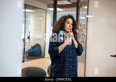 Nachdenkliche Geschäftsfrau mit Haftnotizen am im Büro stehenden Körper Stockfoto