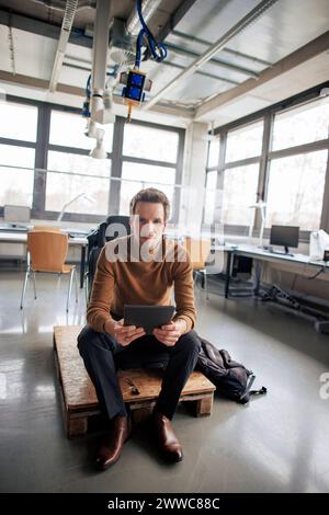 Ingenieur, der in der Werkstatt einen Tablet-PC auf dem Stuhl hält Stockfoto