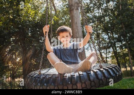 Lächelnder Junge, der im Park auf Reifen schwingt Stockfoto