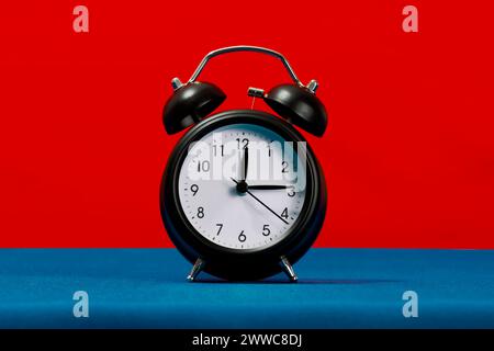 Schwarzer Retro-Wecker vor rotem Hintergrund Stockfoto