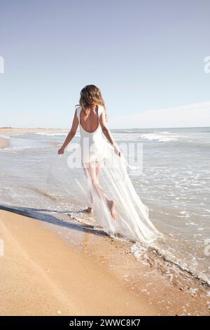 Die junge Braut trägt ein weißes Hochzeitskleid und läuft am Strand Stockfoto