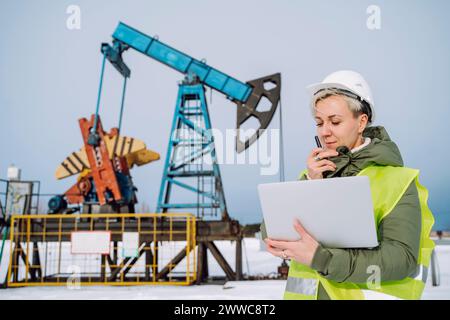 Ein Ingenieur hält einen Laptop und spricht über Walkie-Talkie auf dem Ölfeld Stockfoto