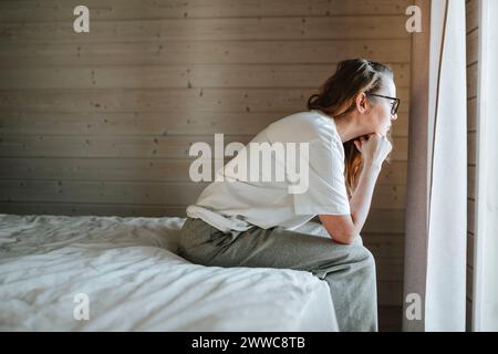 Gestresste Frau, die sich auf Ellbogen stützt und zu Hause aus dem Fenster blickt Stockfoto