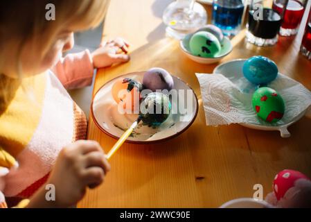 Mädchen malt zu Hause Ostereier auf Teller Stockfoto