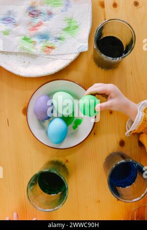 Hand-an-Mädchen, das zu Hause grüne Ostereier aufnimmt Stockfoto