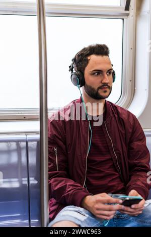 Junger Mann, der im Zug Musik über Kopfhörer hört Stockfoto