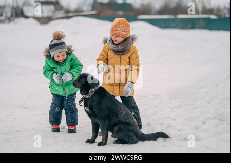 Glückliche Kinder, die warme Kleidung tragen und mit dem Hund im Schnee spielen Stockfoto